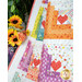 A vibrant quilt featuring colorful patchwork designs with heart motifs, alongside sunflowers in a vase.