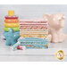 A stack of the fabrics included in the Rainbow Dreams fq set with a Ceramic Elephant and toy rings and a star and thread.