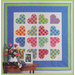 A colorful quilt with heart patterns displayed on a wall, accompanied by a flower arrangement and a photo frame.