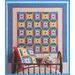 A colorful quilt with a geometric pattern hangs on a blue wall above a bed with decorative pillows.