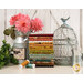 A stack of colorful fabric rolls beside a vintage birdcage, flowers, and sewing spools on a rustic backdrop.