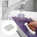 A person holds a purple Panasonic iron while filling it with water from a faucet.