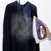 A hand operates a steam iron on a hanging dark blouse, emitting steam for wrinkle removal.