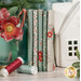 A stack of fabrics featured in the Merry Little Christmas - Duck Egg fat quarter set, with a glass and flowers and a candy cane and a house and thread.