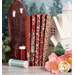 A stack of the fabrics included in the Merry Little Christmas - Red fat quarter set, with pine trees and flowers and a vase and a house and thread.