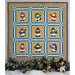 A quilt with 9 unique snowman blocks on a light green top with blue and white sashing, hung on a wall with tree boughs and snowman decorations laid out at the bottom of the frame.