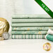 A stack of the six fabrics included in the 6 FQ Set Light Mint/Silver by Stof Fabrics, with thread and ornaments.