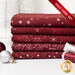 A stack of the five fabrics included in the 5 Half Yard Set Red/Silver by Stof Fabrics, with ornaments and thread.