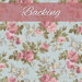 A swatch of light blue fabric with pink roses. A pink banner reads 