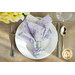 A top down shot of a place setting with the reversible purple paisley fabric of the napkin faced out.