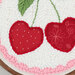 Close up of embroidery design featuring two red cherries with polka dots and floral patterns.