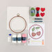 Craft supplies arranged on a light background, including yarn, an embroidery hoop, and a pattern sheet.