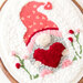 Close up of embroidery design featuring a gnome holding a heart surrounded by florals