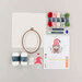 Craft supplies arranged on a light background, including yarn, an embroidery hoop, and a pattern sheet.