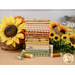 A stack of fabrics included in the Sunflower Whispers FQ set, with sunflowers and a basket and a tin and thread.
