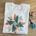 A version of the Charming Applique Double Aster Block, a series of teal, coral, and white fabrics on a white sweatshirt.