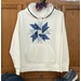 A version of the Charming Applique Double Aster Block, a series of blue fabrics on a white sweatshirt.