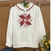 A version of the Charming Applique Double Aster Block, a series of red fabrics on a white sweatshirt.