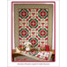 A decorative quilt hangs over a table with a matching runner, featuring red, green, and floral patterns.