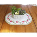 A woven basket with decorative plants sits on a round table mat with pink floral patterns.