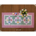 A floral table runner with pastel colors and a vase of tulips on a wooden table surface.