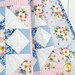 Colorful quilt featuring floral patterns, geometrical designs, and varied fabrics in soft blues and pinks.