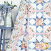 A patchwork quilt featuring a geometric design with floral patterns in white, pink, and blue drapes over a chair, next to a vase with blue flowers.