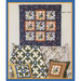 Colorful quilt hanging on a wall with coordinating decorative pillows displayed on a white chair.