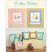 Image features two colorful quilts with animal designs hanging on the wall, surrounded by cushions and a teddy bear.