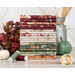 A stack of the fabrics included in the Harvest Bouquet collection, with a jug and wheat and leaves and pumpkins and thread.