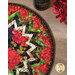 Colorful round table mat featuring red flowers, green leaves, and a zigzag border on a wooden surface.