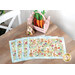 Set of decorative placemats featuring rabbits and flowers, alongside a pink basket with carrots and a bunny figurine on a wooden table.