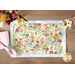 A decorative placemat featuring colorful illustrations of rabbits among vibrant flowers, set on a wooden table.