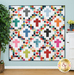 A colorful quilt featuring cross patterns in various hues on a soft background, displayed on a wall.