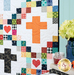 A colorful patchwork quilt featuring crosses and hearts on a white background, next to a floral vase. .