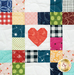 A close-up of a quilt featuring a central red heart among various patterned squares in a grid layout.