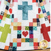 Colorful quilt featuring a pattern of crosses, hearts, and squares in various fabrics on a white background.