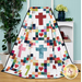 Colorful quilt featuring a cross and heart pattern, displayed next to a plant and a table with decor. 