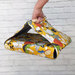 A hand holding a colorful fabric tote bag with a vegetable print, set against a light brick background.