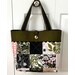 The completed Charming Tote bag in  brown, black, pink, and green fabrics, hung on a white closet door handle.