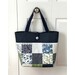 The completed Charming Tote bag in navy, white, blue, and green fabrics, hung on a white closet door handle.