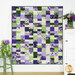 The completed Ten Square Scramble Quilt, colored in bright purple, cream, and green fabrics from the Georgina collection, hung on a white paneled wall and staged with coordinating flowers and furniture.