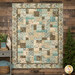 A patchwork quilt displayed on a wood-paneled wall, featuring nature inspired patterns in the soft browns and blues of the Nature's Landscapes collection.