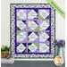 The completed Forever Sisters Charm Quilt colored in vibrant purple, green, and cream fabrics from the Georgina collection, hung on a cream paneled wall above a gray armoire, staged with coordinating decor.