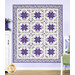 A floral-patterned quilt featuring green and purple colors with a geometric design, hung on a lilac-paneled wall and staged with coordinating decor and florals.