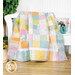 A colorful patchwork quilt draped over a white bench, with a floral vase in the background.