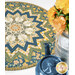 A table topper with a floral and bee pattern, beside a blue teapot and a vase of yellow flowers.