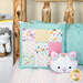 The quillow completely folded into it's case, staged on a bed next to a cat plushie and coordinating decor. 