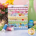 A stack of the fabrics included in the Spring Cheer FQ bundle, with flowers and vases and easter grass and bunnies and eggs and thread.