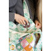 A model holds the midi bag over their shoulder while putting away scissors into one of the dimensional pockets, demonstrating size and function.